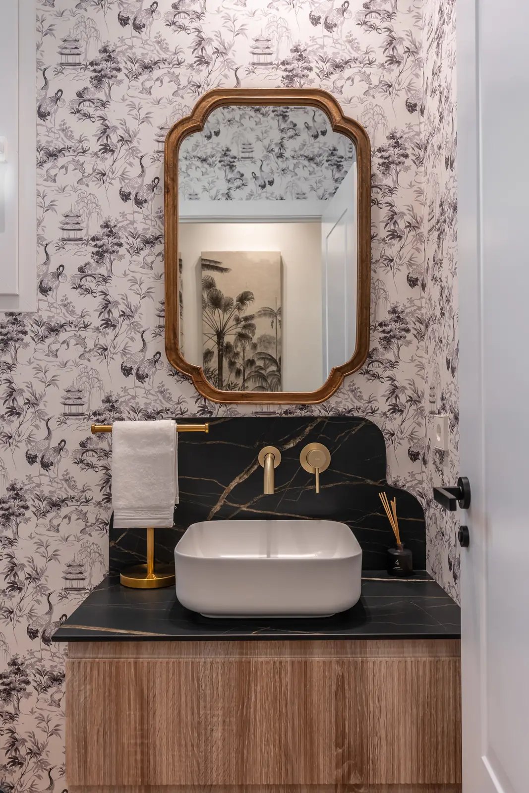 Aseo de cortesía con papel toile, espejo dorado y lavabo sobre mármol negro