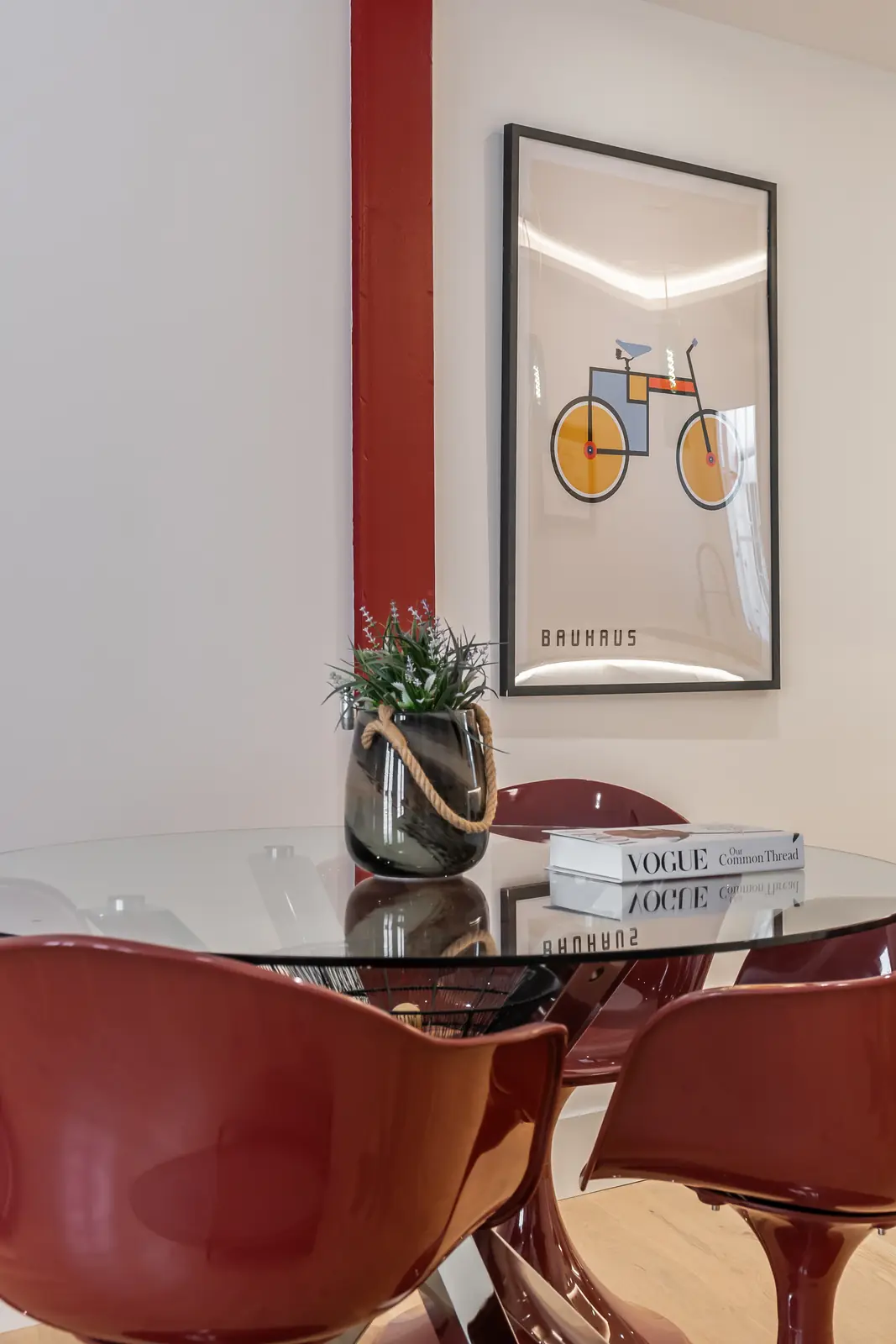 Comedor con mesa de cristal, sillas rojas y lámina Bauhaus enmarcada