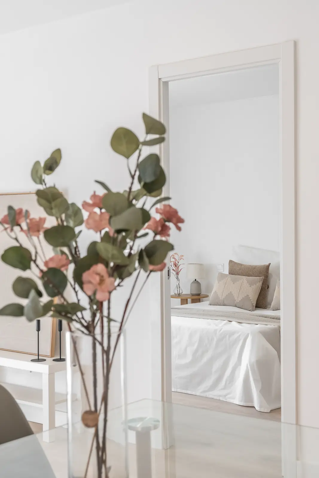 Acceso a dormitorio con cama vestida en blanco y ramas decorativas