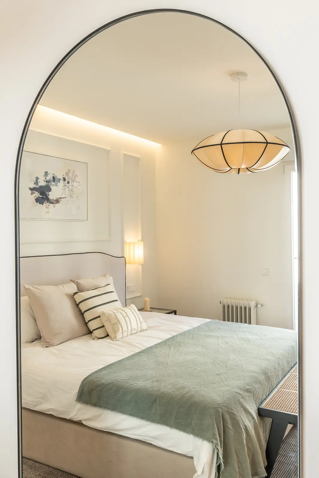 Dormitorio reflejado en espejo con arco y cama con manta verde
