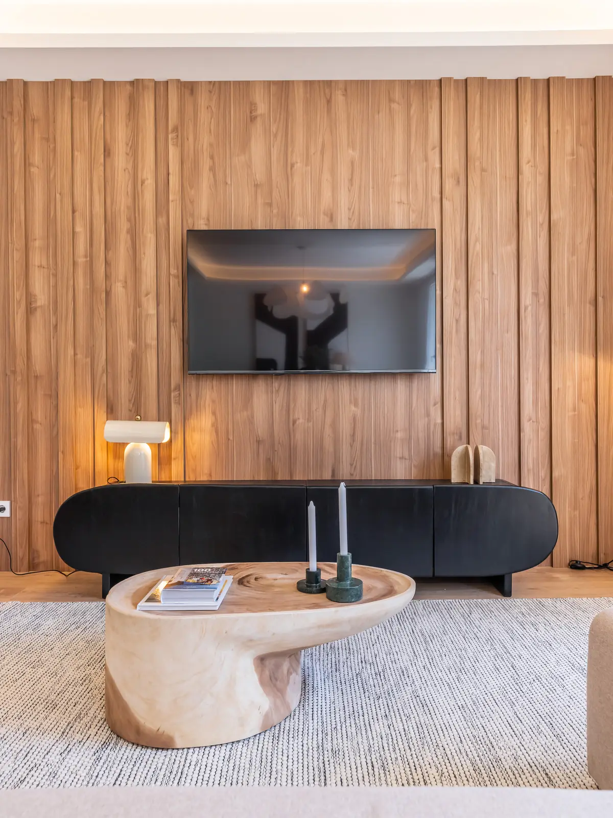 Salón con panel de madera, televisión y mesa de centro de formas orgánicas