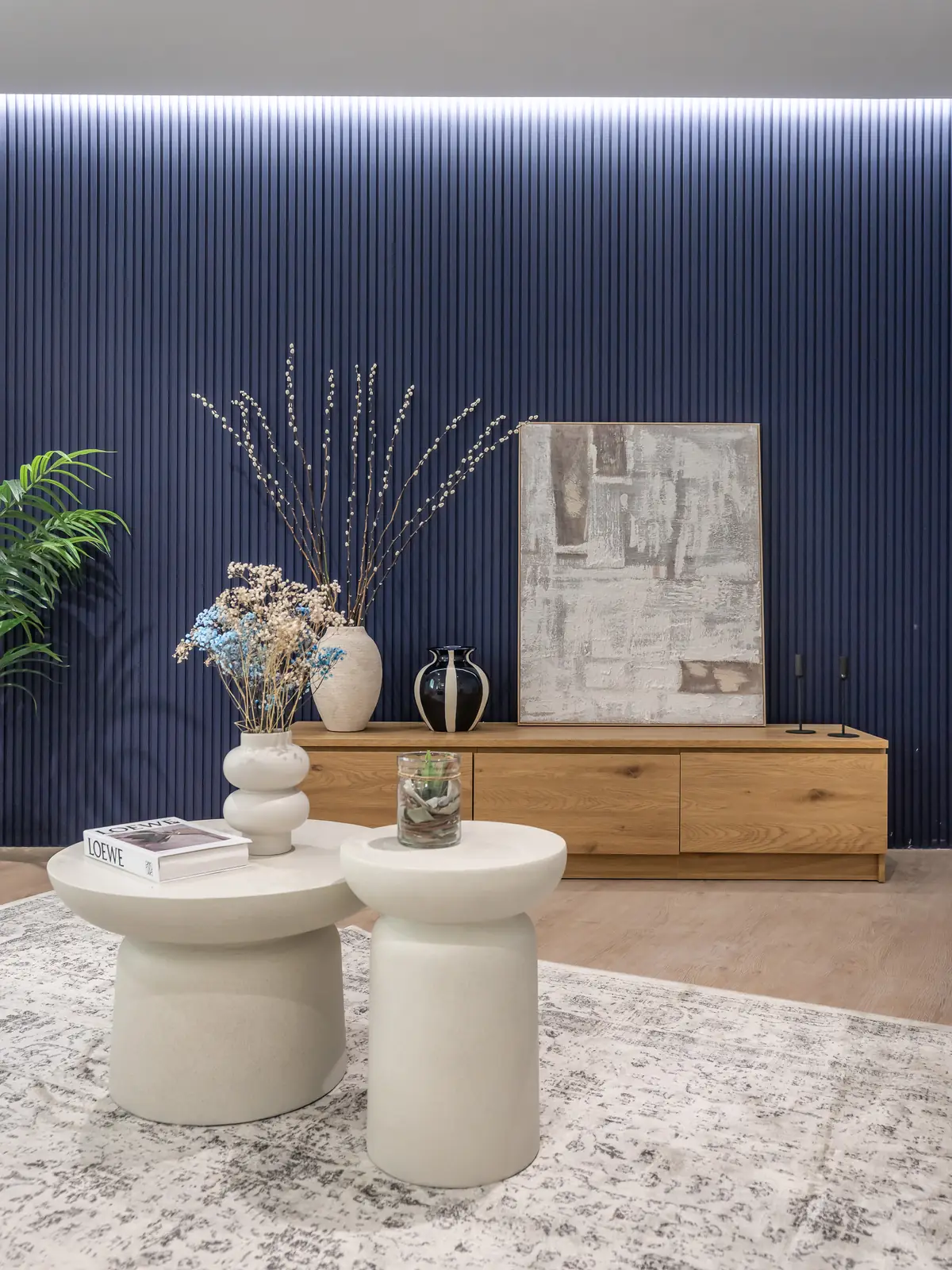 Salón con pared azul estriada, aparador de madera y mesas nido blancas