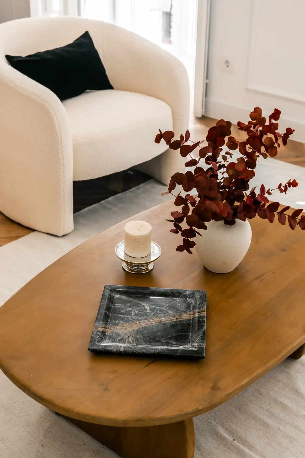 Sillón bouclé blanco junto a mesa de madera con centro decorativo